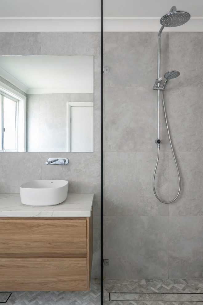 Design ideas for a medium sized contemporary ensuite bathroom in Sydney with flat-panel cabinets, light wood cabinets, a corner bath, a walk-in shower, a one-piece toilet, grey tiles, porcelain tiles, grey walls, marble flooring, a vessel sink, engineered stone worktops, grey floors, an open shower, white worktops, double sinks and a floating vanity unit.