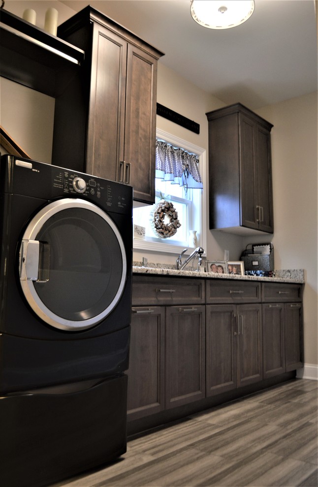 Design ideas for a mid-sized traditional l-shaped utility room in Chicago with an undermount sink, shaker cabinets, solid surface benchtops, beige walls, vinyl floors, a side-by-side washer and dryer, grey floor and dark wood cabinets.