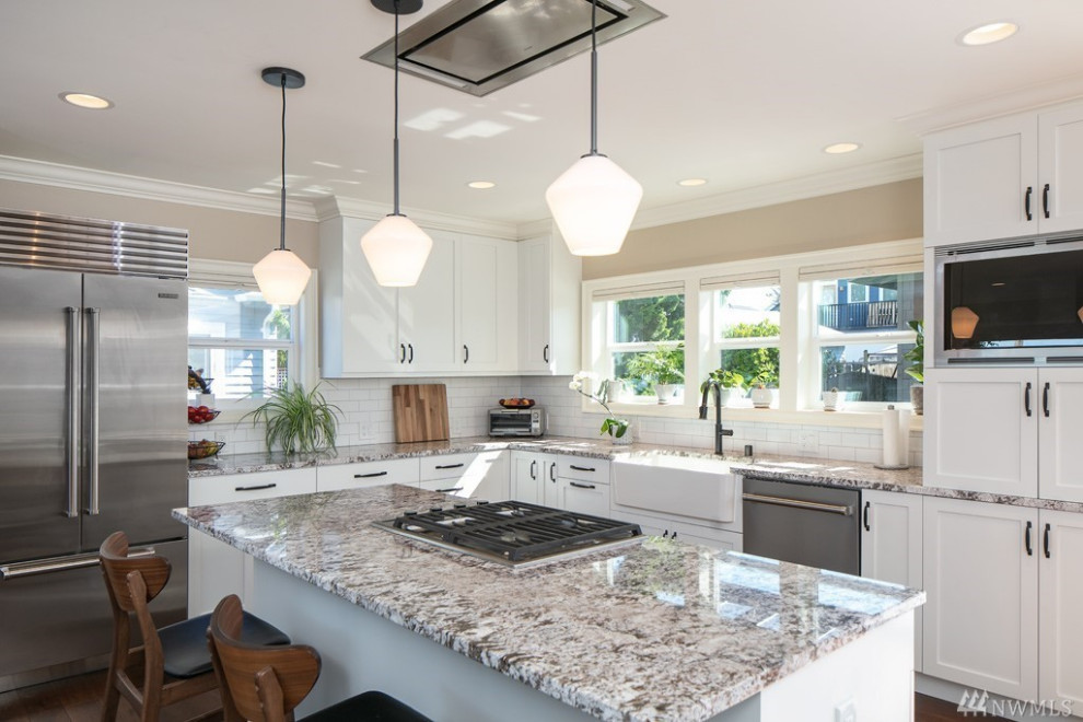 Eat-in kitchen - mid-sized transitional l-shaped medium tone wood floor and brown floor eat-in kitchen idea in Seattle with a farmhouse sink, shaker cabinets, white cabinets, quartz countertops, white backsplash, ceramic backsplash, stainless steel appliances, an island and beige countertops
