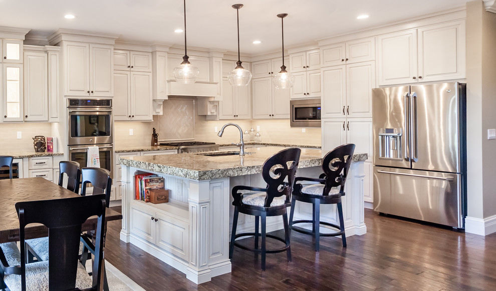 Inspiration for a large transitional l-shaped kitchen remodel in St Louis with an undermount sink, raised-panel cabinets, white cabinets, granite countertops, beige backsplash, subway tile backsplash, stainless steel appliances and an island