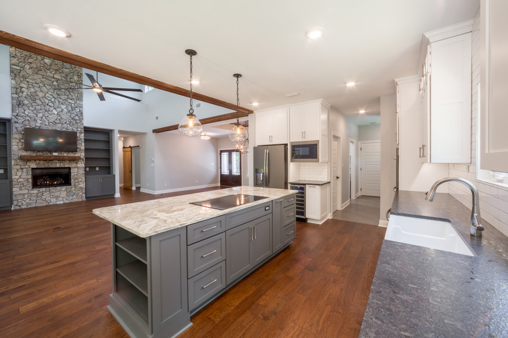 Mid-sized elegant galley medium tone wood floor and brown floor eat-in kitchen photo with a farmhouse sink, recessed-panel cabinets, white cabinets, quartzite countertops, white backsplash, glass tile backsplash, stainless steel appliances, an island and multicolored countertops