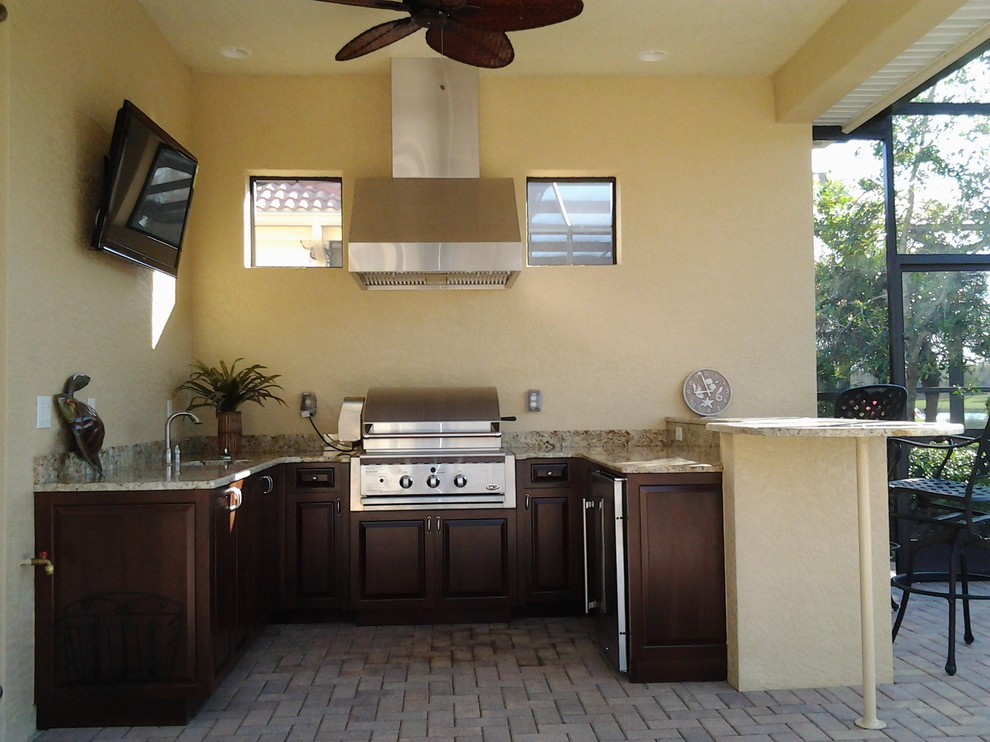 This is an example of a small tropical u-shaped kitchen in Miami with an undermount sink, raised-panel cabinets, dark wood cabinets, granite benchtops, beige splashback, stone slab splashback, stainless steel appliances, brick floors and a peninsula.