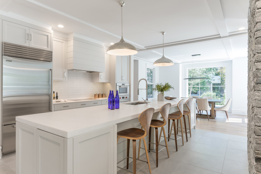 Inspiration for a farmhouse galley ceramic tile and gray floor eat-in kitchen remodel in New York with shaker cabinets, white cabinets, marble countertops, white backsplash, ceramic backsplash, stainless steel appliances, an island, white countertops and an undermount sink