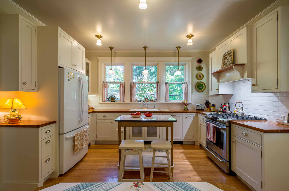 Klassisk inredning av ett avskilt, mellanstort brun brunt u-kök, med en nedsänkt diskho, luckor med infälld panel, vita skåp, träbänkskiva, vitt stänkskydd, stänkskydd i keramik, vita vitvaror, ljust trägolv, en köksö och brunt golv