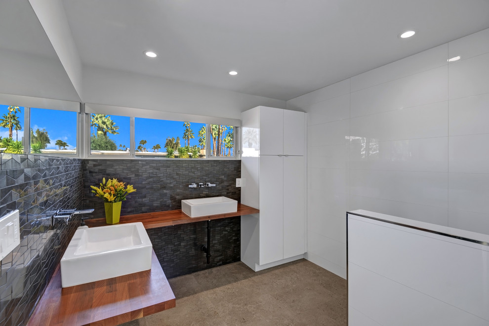 Inspiration for a mid-sized midcentury master bathroom in Los Angeles with flat-panel cabinets, white cabinets, a curbless shower, white tile, stone tile, white walls, porcelain floors, a vessel sink and wood benchtops.
