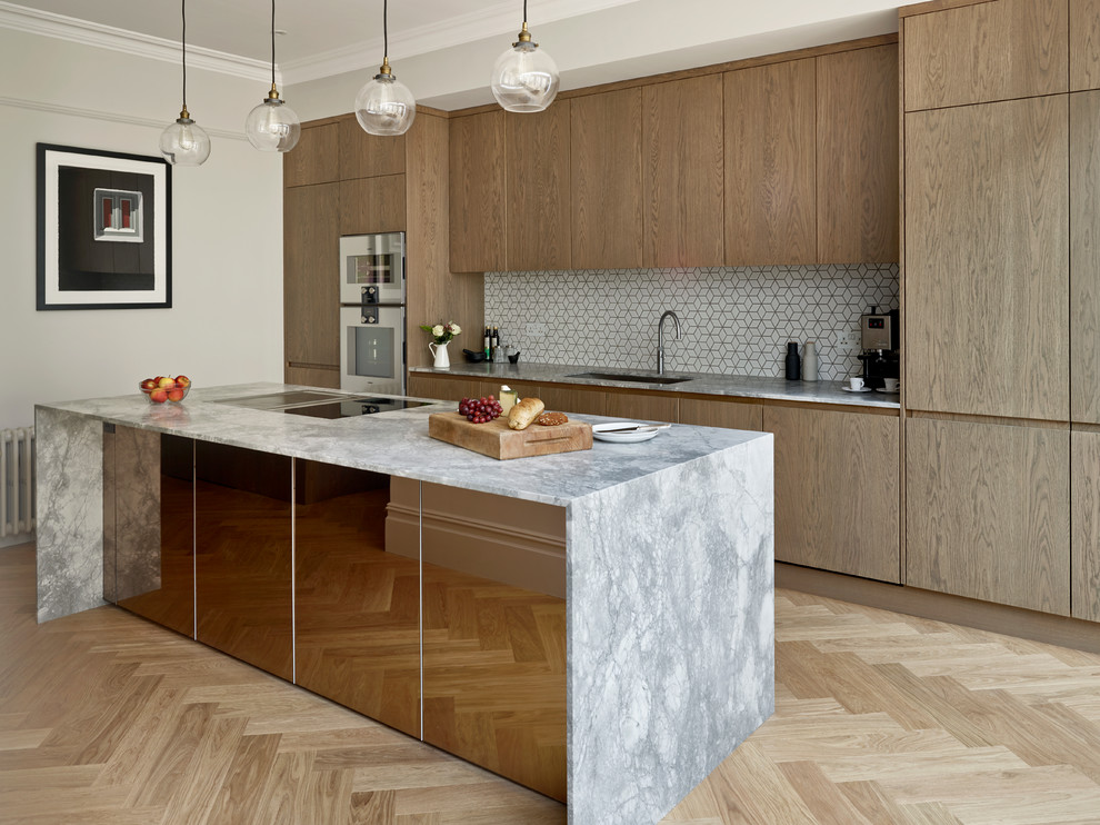 This is an example of a contemporary galley kitchen in London with an undermount sink, flat-panel cabinets, medium wood cabinets, white splashback, mosaic tile splashback, stainless steel appliances, light hardwood floors and with island.