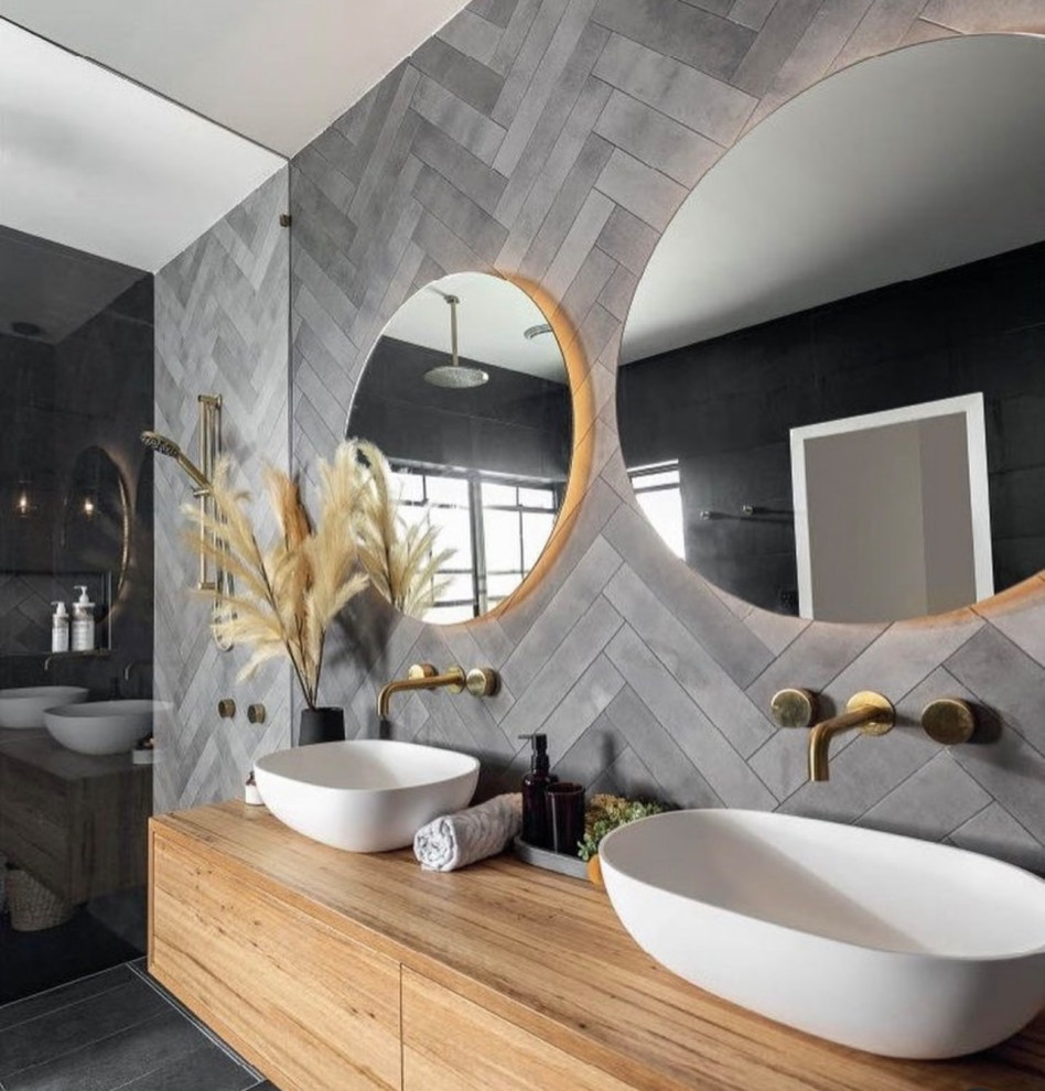 This is an example of a large ensuite bathroom in Dallas with flat-panel cabinets, medium wood cabinets, grey tiles, cement tiles, grey walls, ceramic flooring, a vessel sink, engineered stone worktops, black floors, a hinged door, brown worktops, a feature wall, double sinks, a built in vanity unit and a timber clad ceiling.