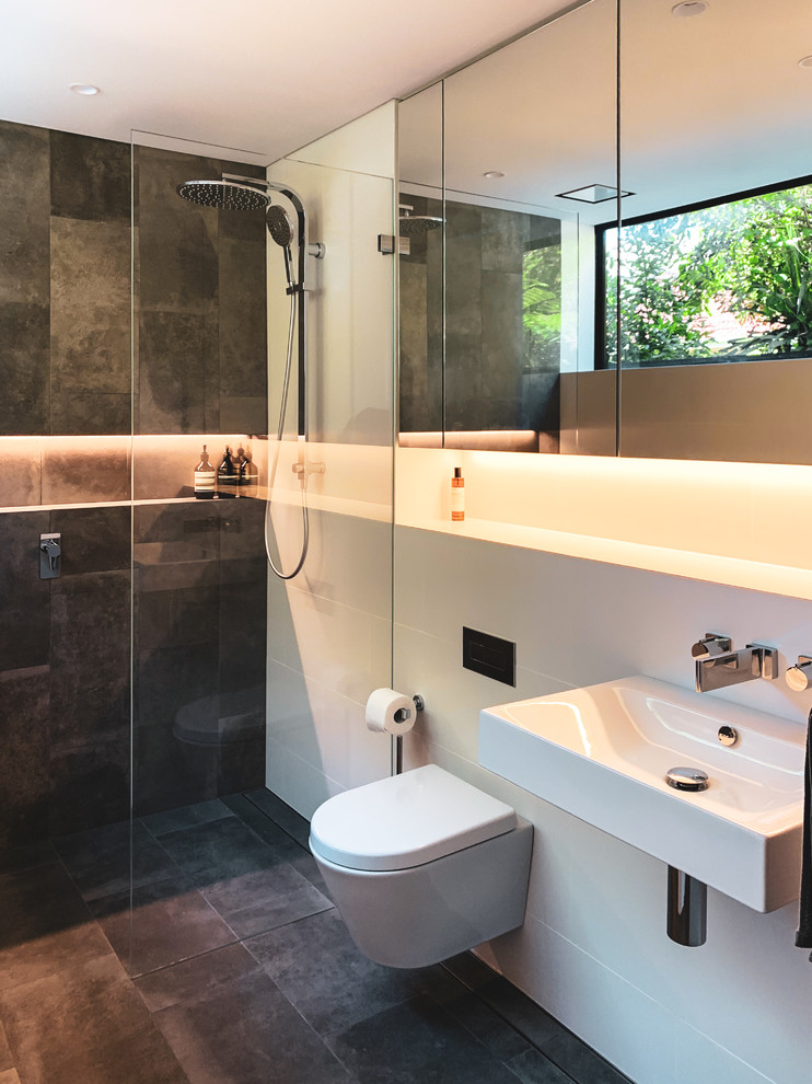 This is an example of a contemporary bathroom in Sydney with a curbless shower, a wall-mount toilet, gray tile, white tile, white walls, a wall-mount sink, grey floor and an open shower.