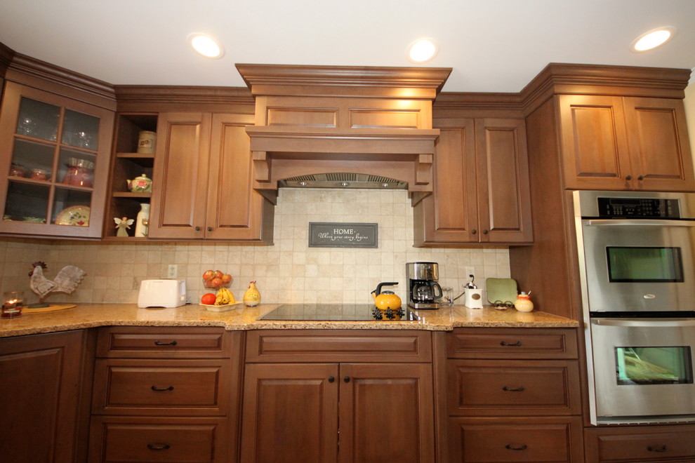 This is an example of a mid-sized traditional l-shaped separate kitchen in New York with an undermount sink, raised-panel cabinets, dark wood cabinets, granite benchtops, beige splashback, stone tile splashback, stainless steel appliances, ceramic floors, with island and brown floor.