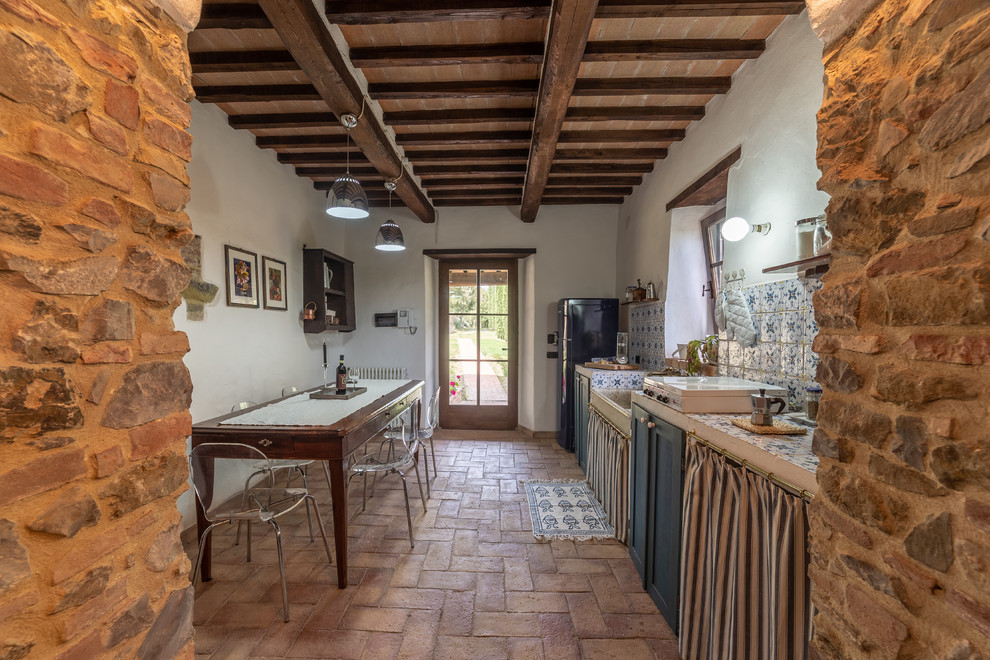 Photo of a country single-wall eat-in kitchen in Florence with a farmhouse sink, shaker cabinets, blue cabinets, tile benchtops, multi-coloured splashback, brick floors, no island, brown floor, multi-coloured benchtop and black appliances.