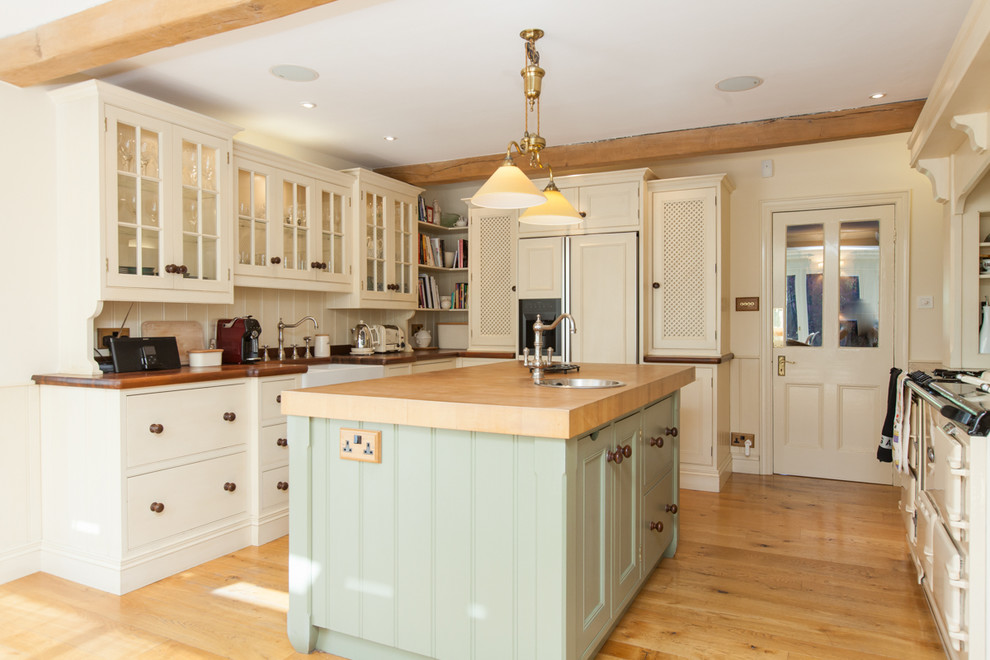 Design ideas for a mid-sized country kitchen in Belfast with a farmhouse sink, flat-panel cabinets, white cabinets, wood benchtops, panelled appliances, medium hardwood floors, with island and beige floor.