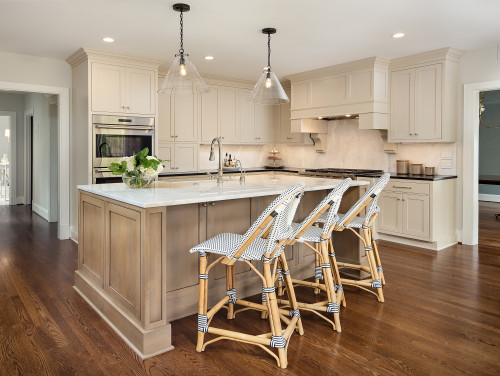 Warm beige kitchen cabinets with a large island, marble countertop and wood flooring in a bright open-concept kitchen