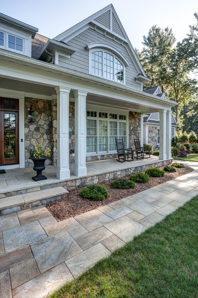 Design ideas for a large traditional front yard verandah in Boston with natural stone pavers and a roof extension.