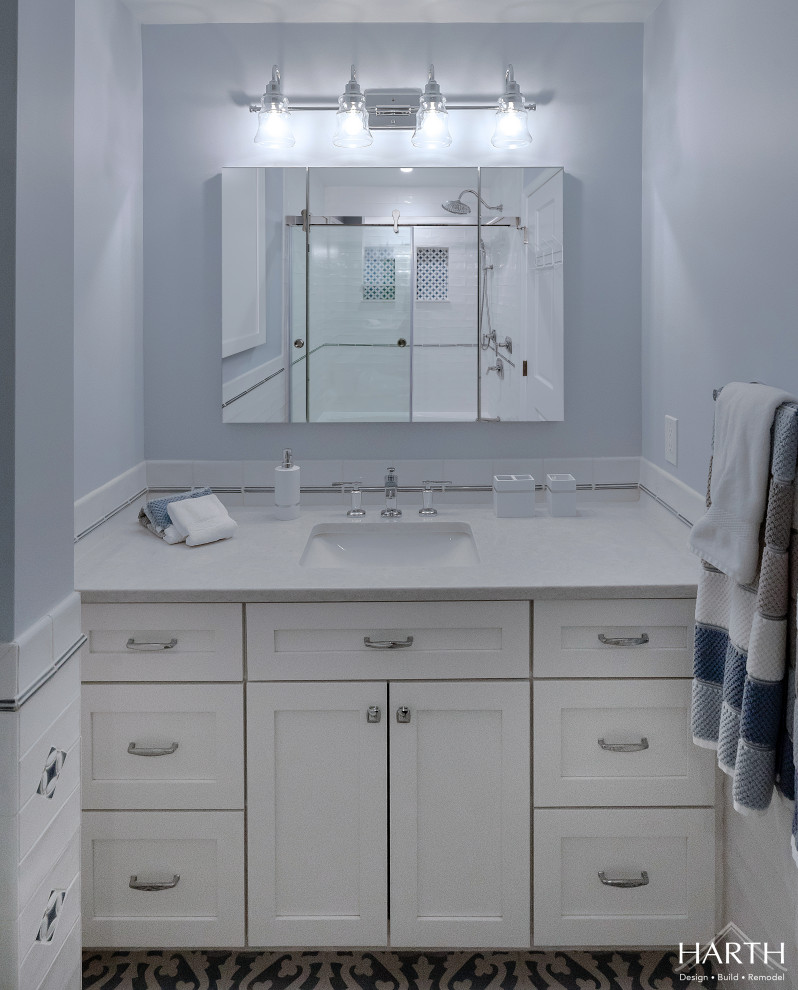 Photo of a mid-sized traditional kids bathroom in Philadelphia with shaker cabinets, white cabinets, an alcove tub, a shower/bathtub combo, a two-piece toilet, white tile, subway tile, blue walls, cement tiles, an undermount sink, engineered quartz benchtops, grey floor, a sliding shower screen, grey benchtops, a niche, a single vanity, a built-in vanity and decorative wall panelling.