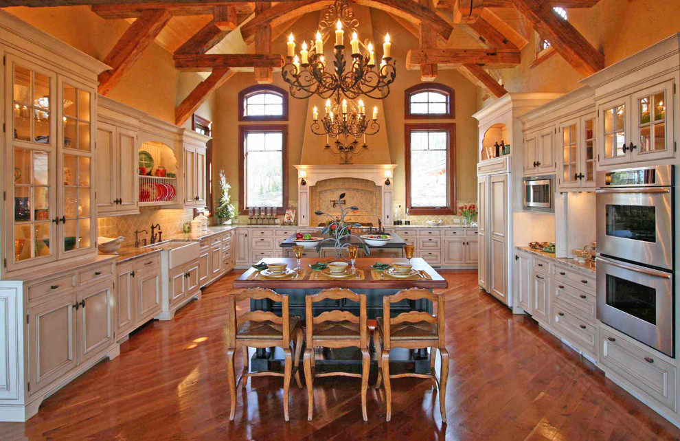 Inspiration for an expansive country u-shaped eat-in kitchen in Other with a farmhouse sink, raised-panel cabinets, white cabinets, granite benchtops, beige splashback, porcelain splashback, stainless steel appliances, medium hardwood floors and multiple islands.