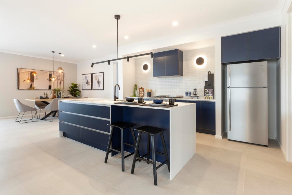 Contemporary single-wall open plan kitchen in Melbourne with an undermount sink, blue cabinets, quartz benchtops, white splashback, ceramic splashback, stainless steel appliances, ceramic floors, with island, beige floor and white benchtop.
