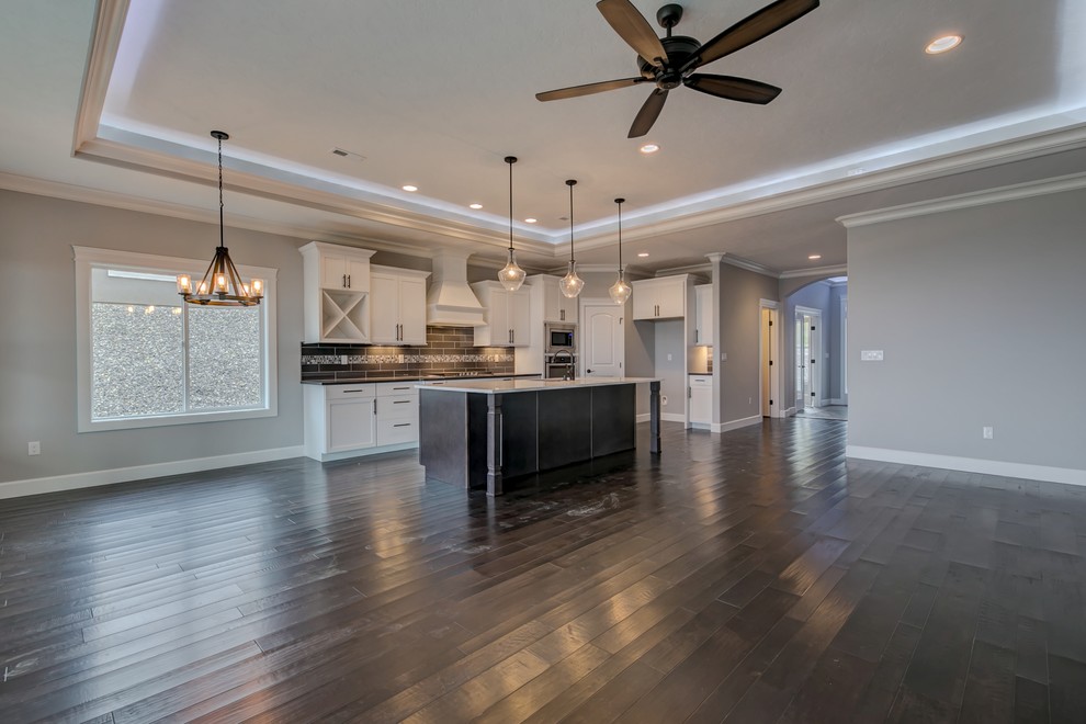 Example of a mid-sized transitional l-shaped medium tone wood floor open concept kitchen design in Seattle with an undermount sink, shaker cabinets, white cabinets, gray backsplash, glass tile backsplash, stainless steel appliances, an island and quartz countertops