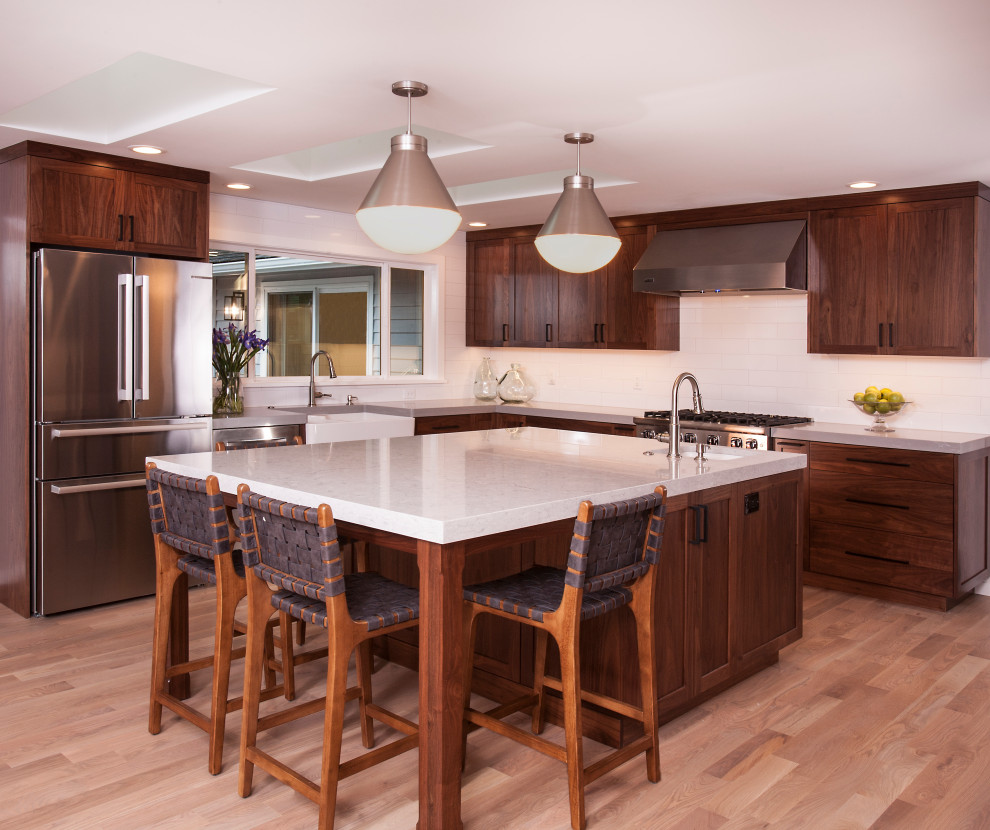 Large transitional u-shaped light wood floor and brown floor eat-in kitchen photo in Seattle with a farmhouse sink, dark wood cabinets, white backsplash, subway tile backsplash, stainless steel appliances, an island and white countertops