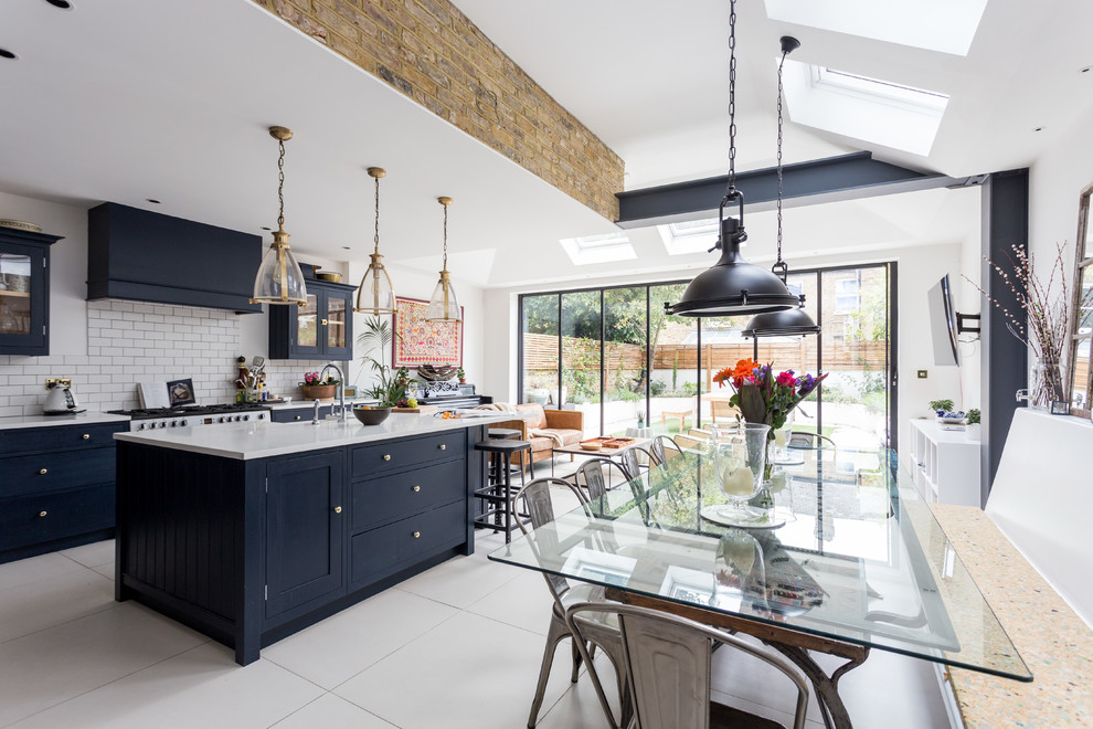 This is an example of a large transitional open plan kitchen in London with white floor, white splashback, subway tile splashback, with island and blue cabinets.