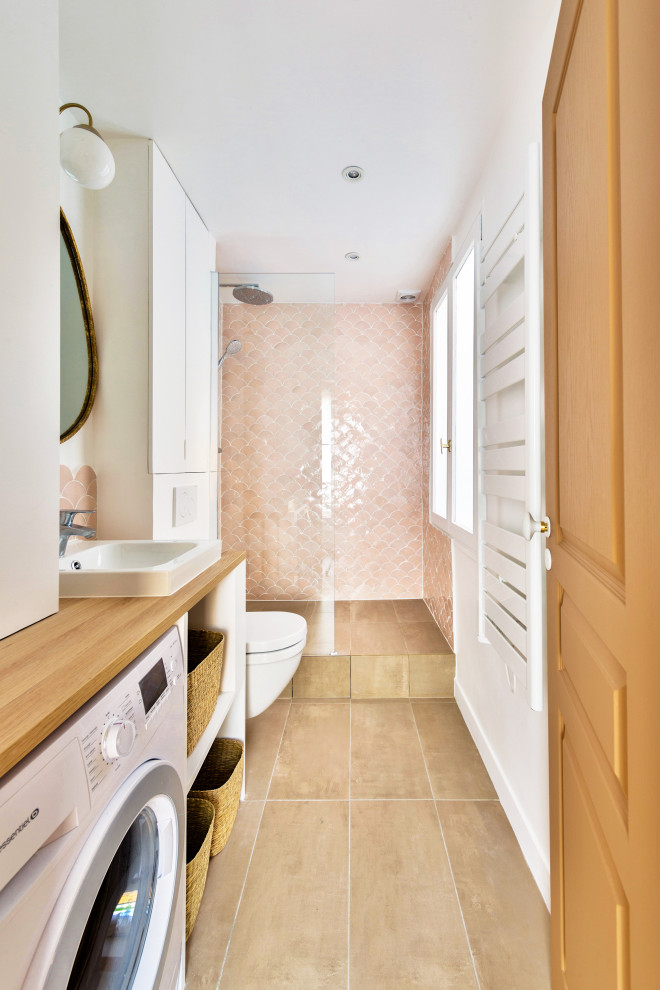 This is an example of a mid-sized traditional 3/4 bathroom in Paris with a curbless shower, an open shower, a single vanity, flat-panel cabinets, white cabinets, a wall-mount toilet, pink tile, white walls, a console sink, wood benchtops, beige floor, a laundry and a built-in vanity.