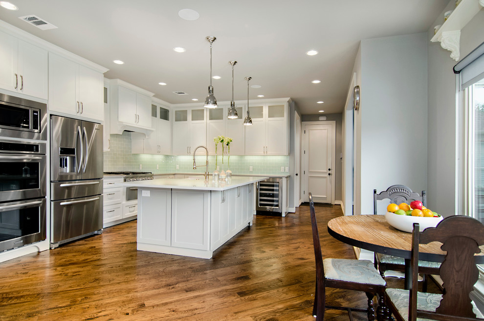 Mid-sized transitional l-shaped eat-in kitchen in Dallas with a farmhouse sink, shaker cabinets, white cabinets, granite benchtops, glass tile splashback, stainless steel appliances and medium hardwood floors.