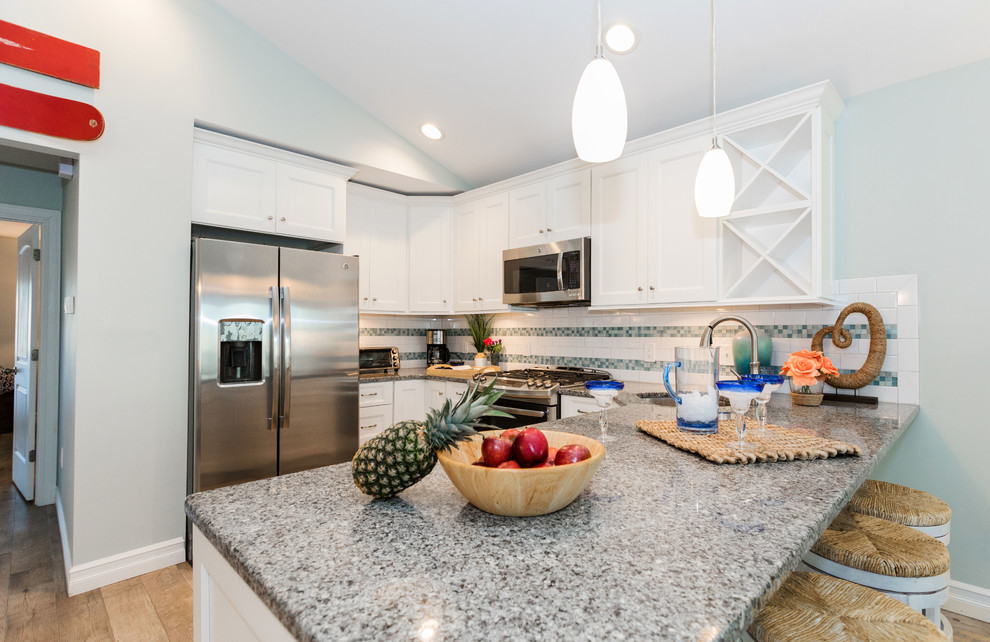 Inspiration for a mid-sized beach style u-shaped eat-in kitchen in Philadelphia with shaker cabinets, white cabinets, wood benchtops, yellow splashback, ceramic splashback, stainless steel appliances, light hardwood floors, with island, brown floor and grey benchtop.