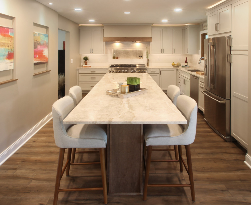 Eat-in kitchen - mid-sized transitional l-shaped brown floor eat-in kitchen idea with an undermount sink, shaker cabinets, white cabinets, quartzite countertops, white backsplash, ceramic backsplash, stainless steel appliances, an island and beige countertops