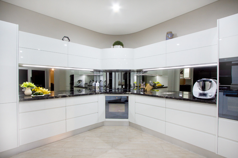 Photo of a large modern l-shaped kitchen pantry in Sunshine Coast with an undermount sink, granite benchtops, mirror splashback, black appliances, porcelain floors, white floor and black benchtop.