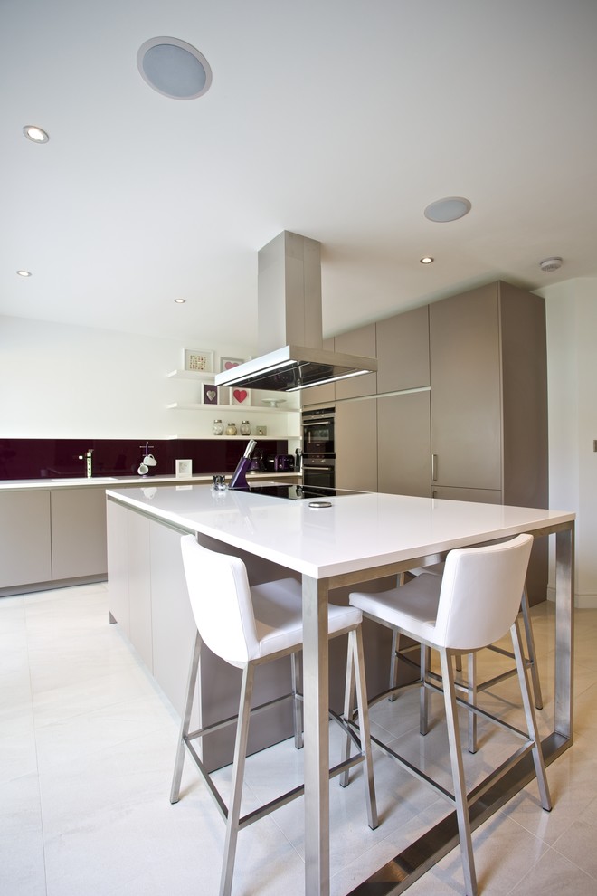 This is an example of a mid-sized contemporary u-shaped eat-in kitchen in Hampshire with an integrated sink, flat-panel cabinets, grey cabinets, solid surface benchtops, blue splashback, glass sheet splashback, stainless steel appliances, porcelain floors and with island.
