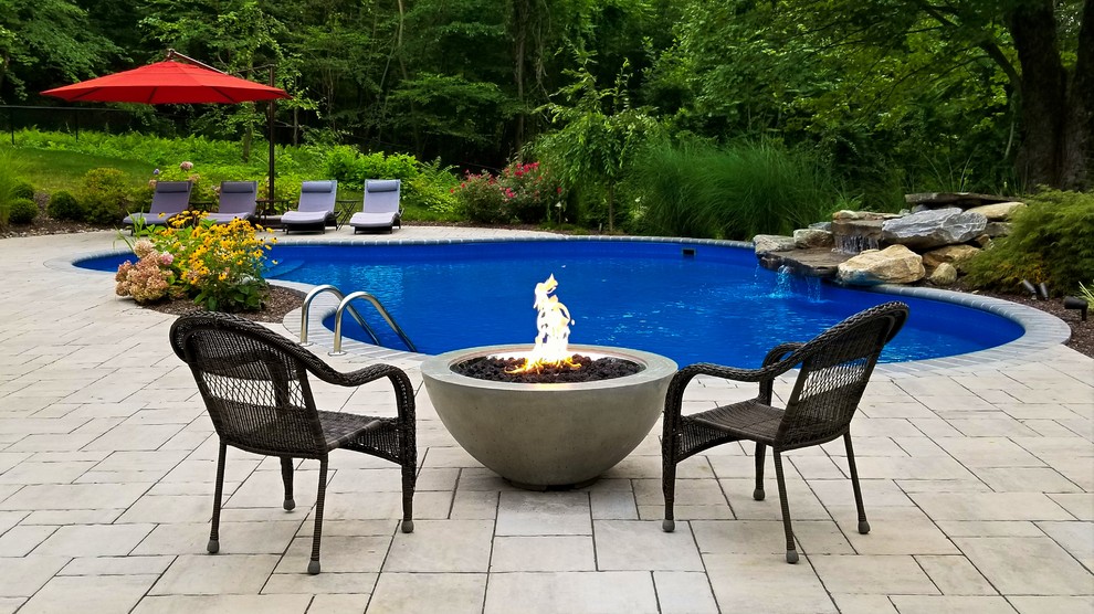 Photo of a mid-sized traditional backyard custom-shaped pool in New York with a water feature and concrete pavers.