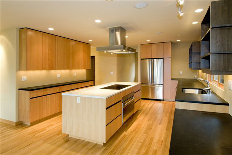 Example of a mid-sized trendy galley carpeted eat-in kitchen design in Seattle with an undermount sink, flat-panel cabinets, light wood cabinets, granite countertops, black backsplash, porcelain backsplash, stainless steel appliances and an island
