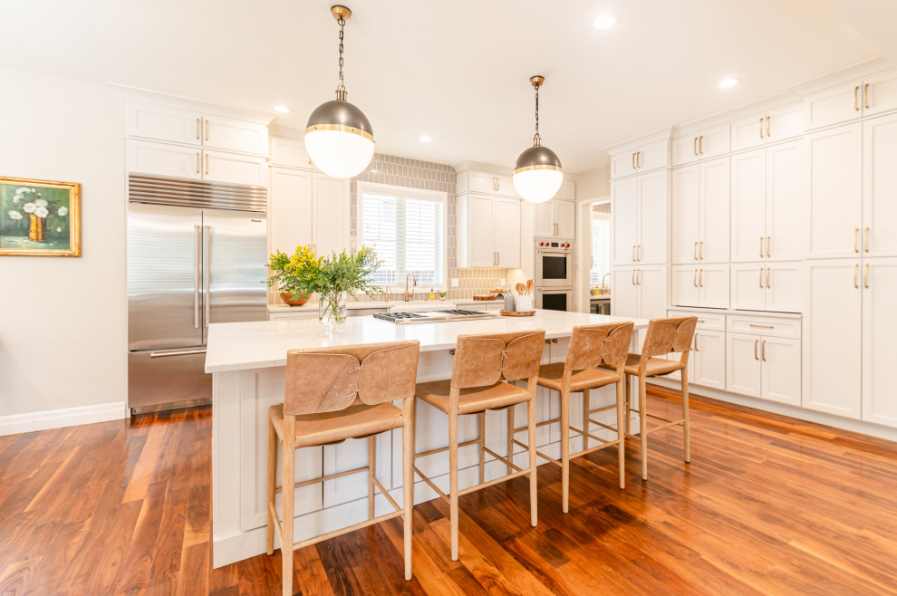 Example of a large transitional l-shaped dark wood floor and brown floor open concept kitchen design in Denver with a farmhouse sink, shaker cabinets, beige cabinets, quartz countertops, beige backsplash, ceramic backsplash, stainless steel appliances, an island and white countertops
