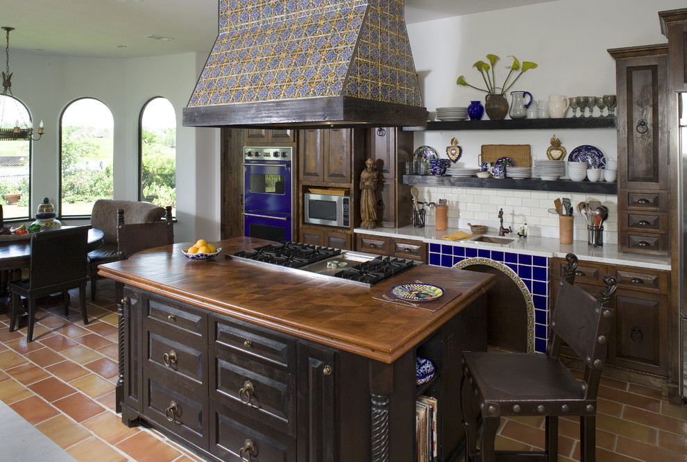 Photo of a mediterranean galley eat-in kitchen in Houston with wood benchtops, an undermount sink, raised-panel cabinets, dark wood cabinets, white splashback, subway tile splashback and coloured appliances.