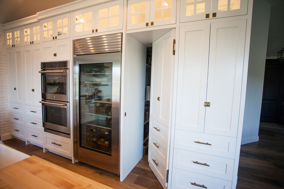 Inspiration for a mid-sized transitional l-shaped medium tone wood floor open concept kitchen remodel in Salt Lake City with a farmhouse sink, shaker cabinets, white cabinets, quartzite countertops, white backsplash, stainless steel appliances and an island