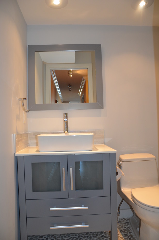 Small transitional 3/4 bathroom in Vancouver with a vessel sink, glass-front cabinets, grey cabinets, solid surface benchtops, a corner shower, a one-piece toilet, beige tile, mosaic tile, grey walls and pebble tile floors.