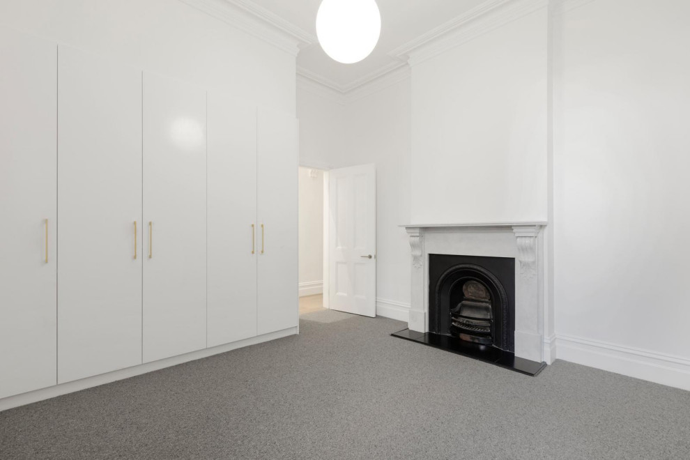 Photo of a mid-sized scandinavian guest bedroom in Melbourne with white walls, carpet, a standard fireplace, a stone fireplace surround and grey floor.
