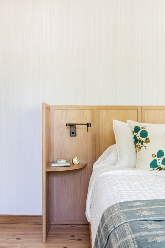 Modelo de dormitorio principal costero de tamaño medio con suelo de madera clara y papel pintado