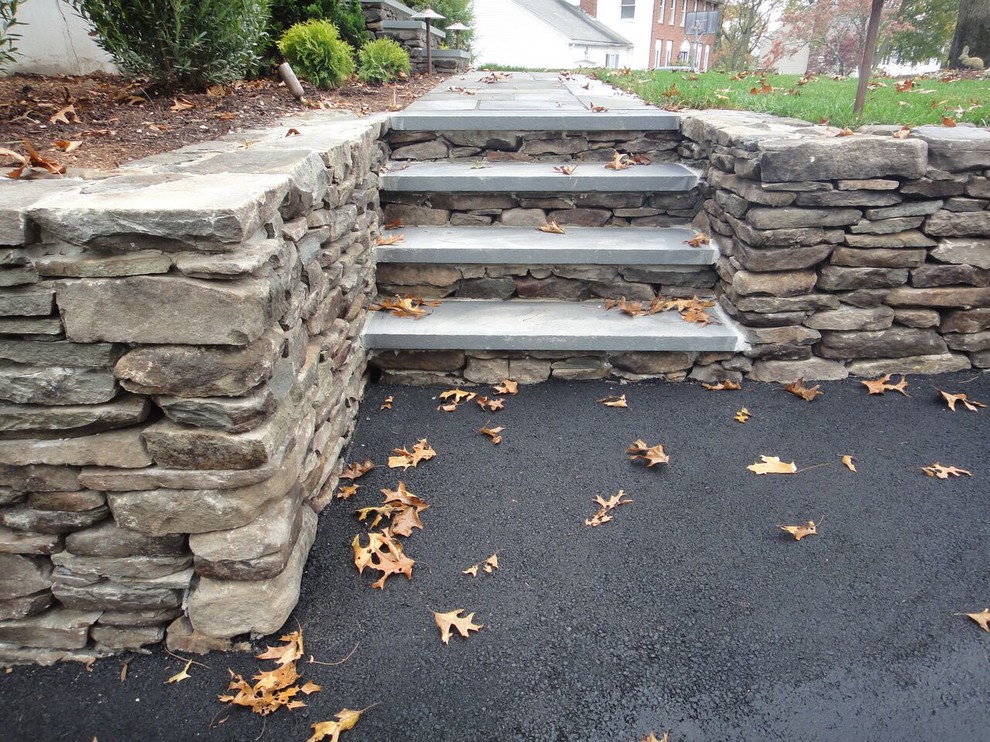 This is an example of a large traditional front yard full sun driveway for fall in Boston with a retaining wall and natural stone pavers.