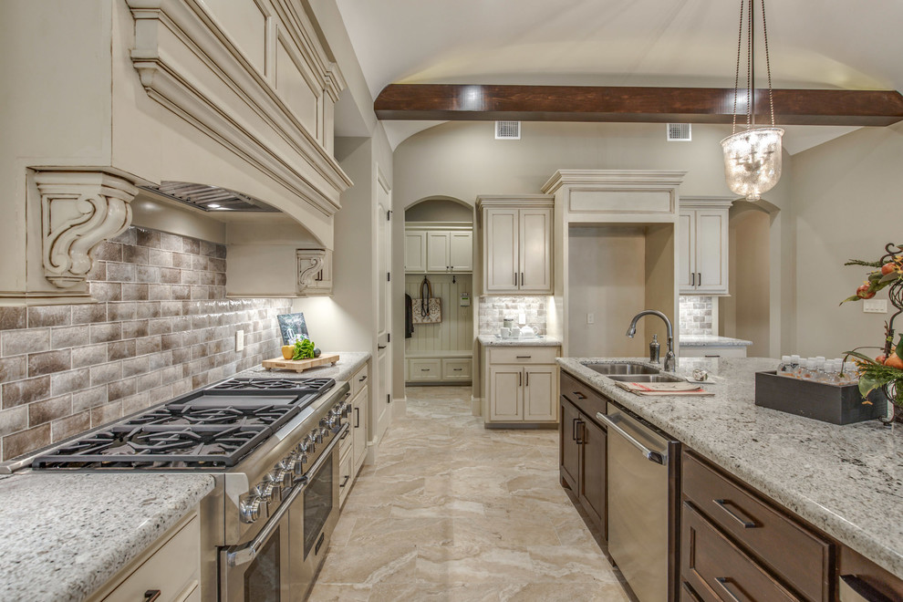 This is an example of a large mediterranean l-shaped eat-in kitchen in Houston with an undermount sink, recessed-panel cabinets, white cabinets, granite benchtops, beige splashback, ceramic splashback, stainless steel appliances, ceramic floors, with island and beige floor.
