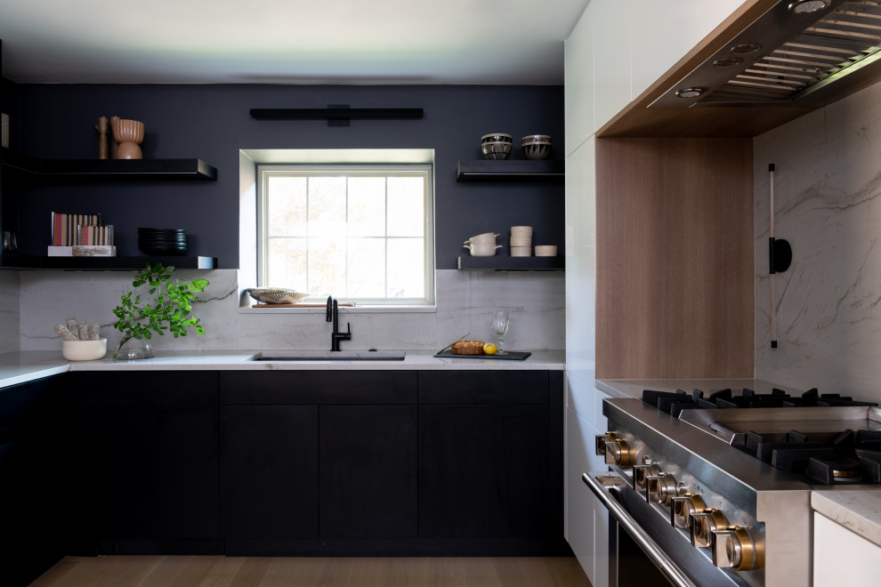 Moderne Küche mit Unterbauwaschbecken, flächenbündigen Schrankfronten, schwarzen Schränken, Küchenrückwand in Weiß, Küchengeräten aus Edelstahl und hellem Holzboden in Dallas