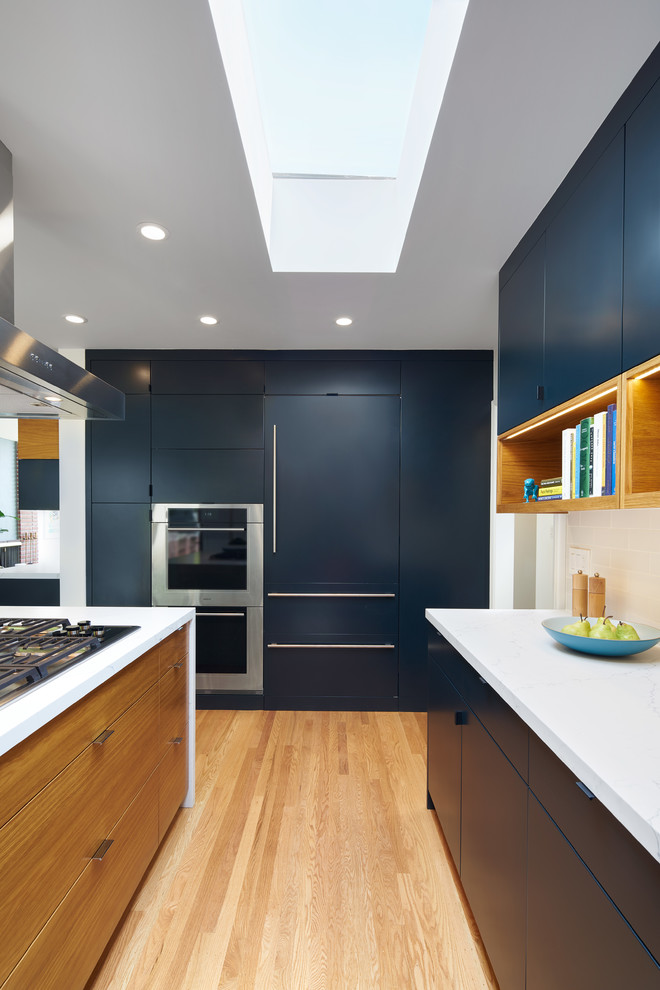 Design ideas for a mid-sized midcentury u-shaped eat-in kitchen in San Francisco with flat-panel cabinets, blue cabinets, quartzite benchtops, panelled appliances, with island, white benchtop, white splashback, subway tile splashback, an undermount sink, light hardwood floors and beige floor.