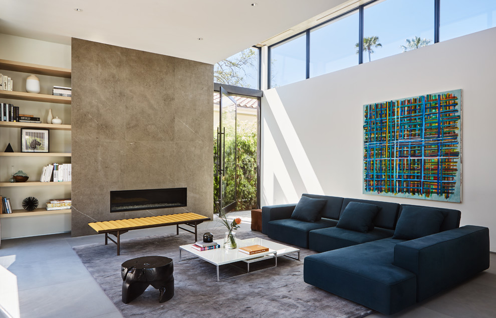 This is an example of a modern living room in Los Angeles with white walls, a ribbon fireplace, a stone fireplace surround and grey floor.