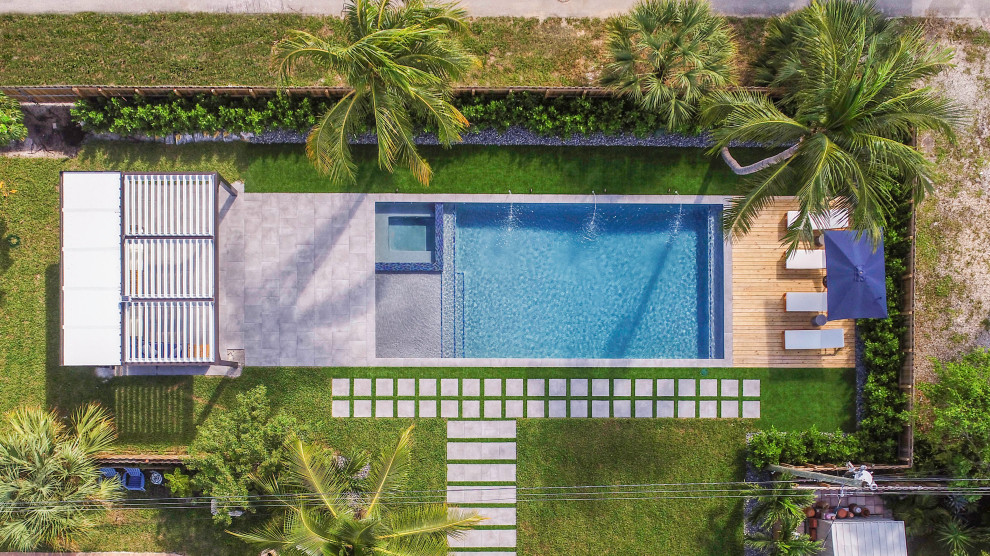 This is an example of a mid-sized modern backyard rectangular lap pool in Miami with a hot tub and decking.