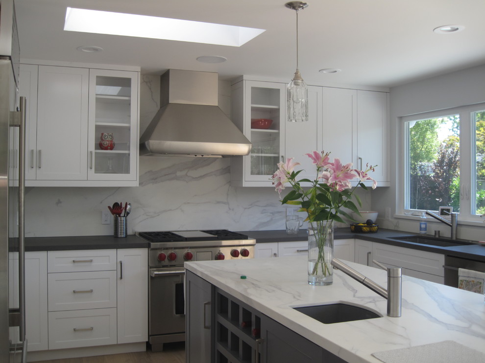 Photo of a large transitional u-shaped separate kitchen in San Francisco with an undermount sink, shaker cabinets, white cabinets, solid surface benchtops, white splashback, stone slab splashback, stainless steel appliances, light hardwood floors and with island.