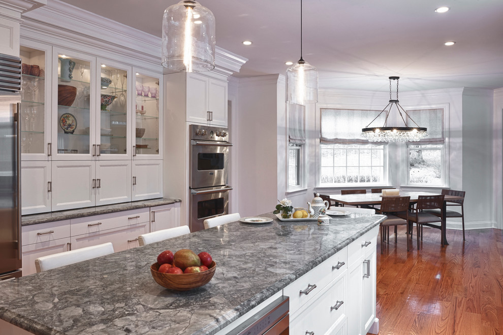 Kitchen pantry - large transitional medium tone wood floor kitchen pantry idea in New York with a farmhouse sink, shaker cabinets, white cabinets, quartzite countertops, white backsplash, mosaic tile backsplash, stainless steel appliances, white walls and an island