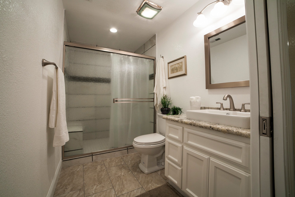 Photo of a mid-sized transitional 3/4 bathroom in Sacramento with recessed-panel cabinets, white cabinets, an alcove shower, a one-piece toilet, a vessel sink, granite benchtops, a sliding shower screen, beige walls and brown floor.