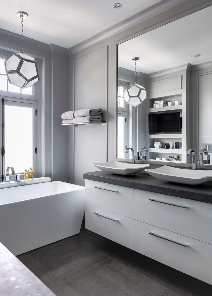 This is an example of a mid-sized contemporary master bathroom in Montreal with flat-panel cabinets, white cabinets, a freestanding tub, a corner shower, a one-piece toilet, gray tile, stone tile, grey walls, porcelain floors, a vessel sink and engineered quartz benchtops.