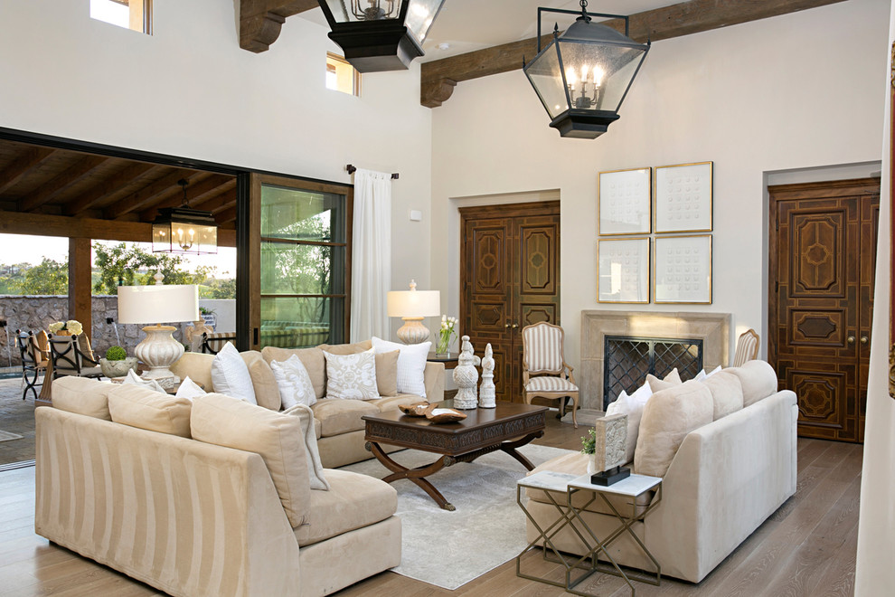 Mediterranean formal open concept living room in San Diego with a stone fireplace surround, white walls, light hardwood floors, a standard fireplace and beige floor.