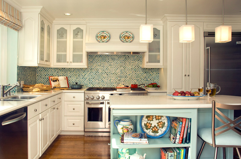 Inspiration for a mid-sized transitional l-shaped open plan kitchen in Los Angeles with a double-bowl sink, raised-panel cabinets, white cabinets, solid surface benchtops, multi-coloured splashback, mosaic tile splashback, stainless steel appliances, medium hardwood floors, with island, brown floor and white benchtop.