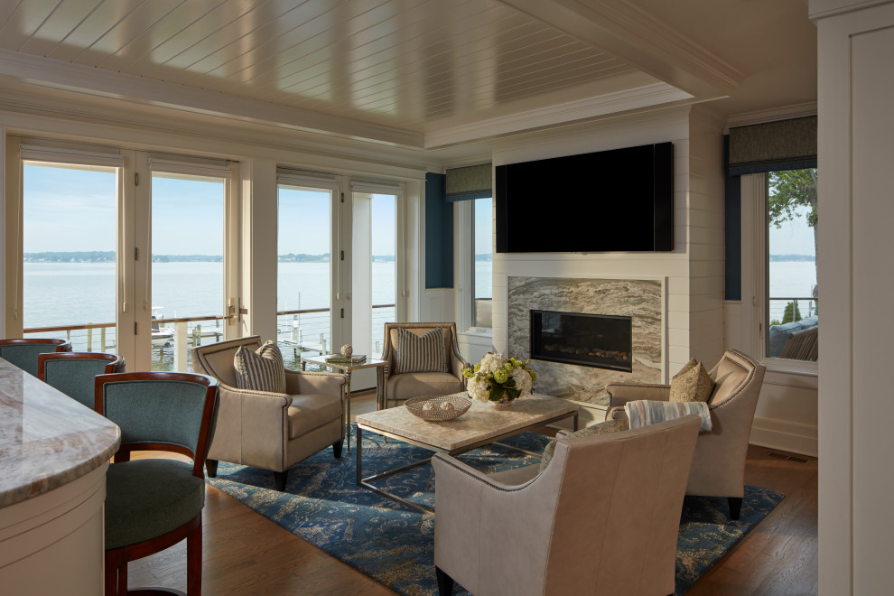 Inspiration for a beach style open concept living room in Baltimore with a home bar, white walls, medium hardwood floors, a hanging fireplace, a stone fireplace surround, a wall-mounted tv and brown floor.